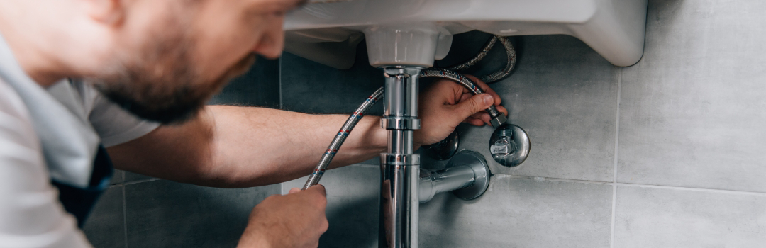 A handyman works on the plumbing of a home.